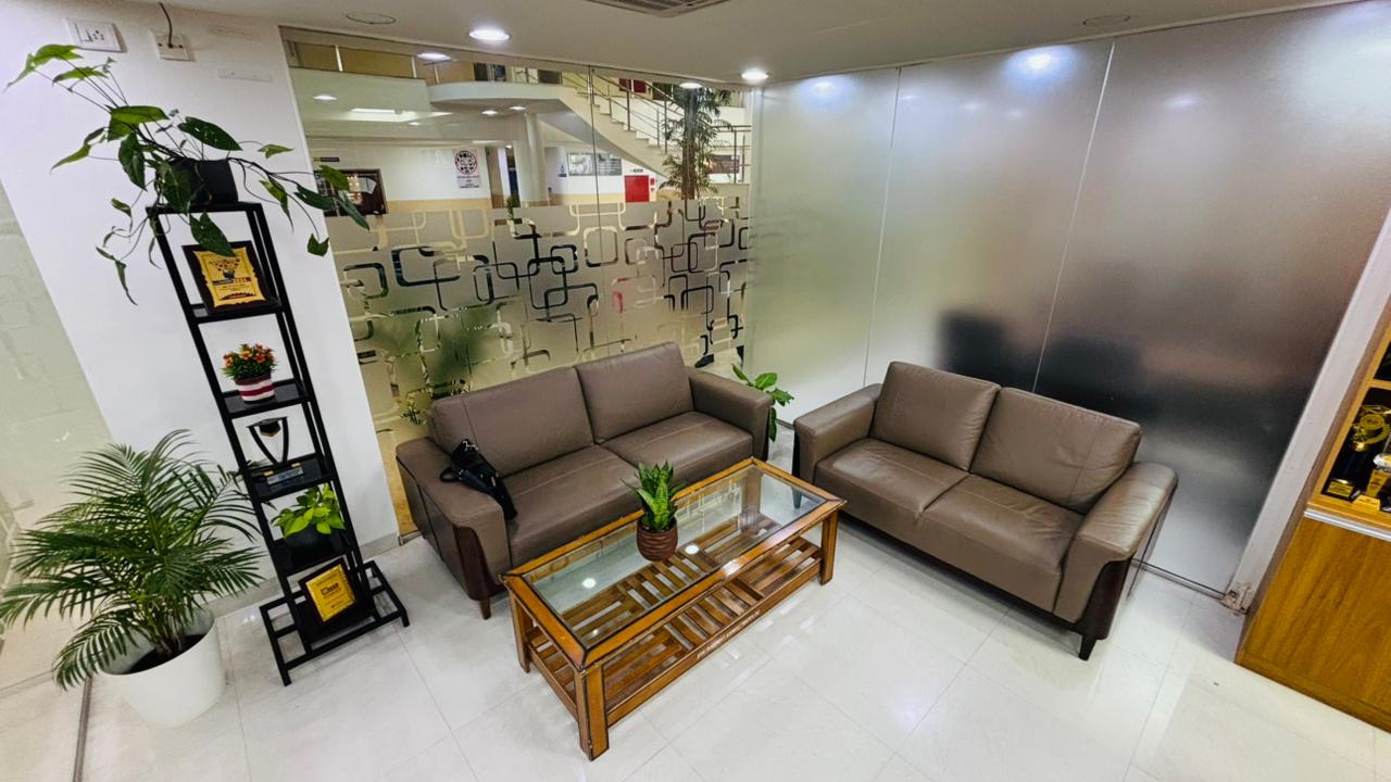 Office waiting lounge with sofas, glass partitions, and plants