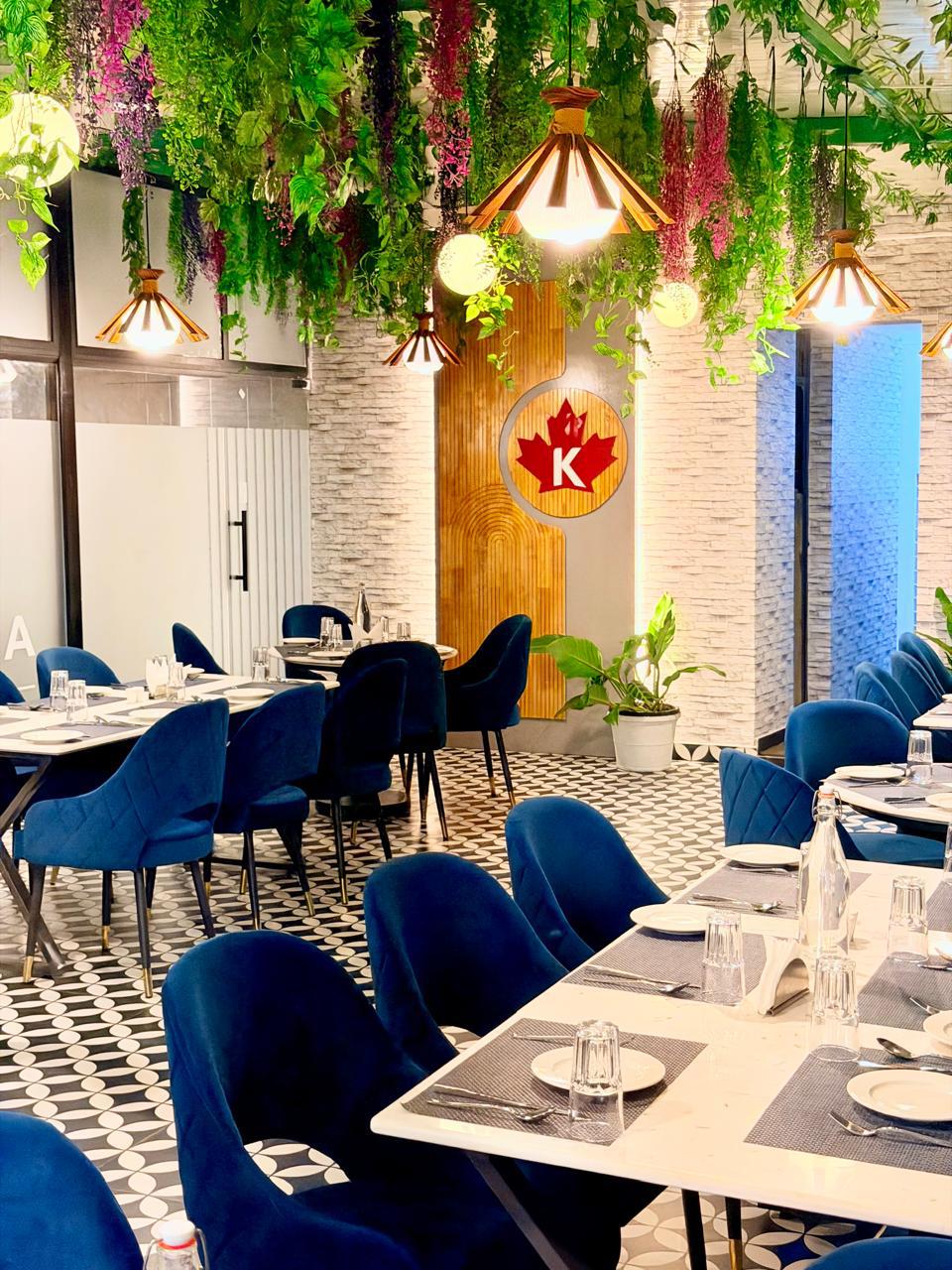Restaurant dining area with blue chairs, greenery, and feature logo wall