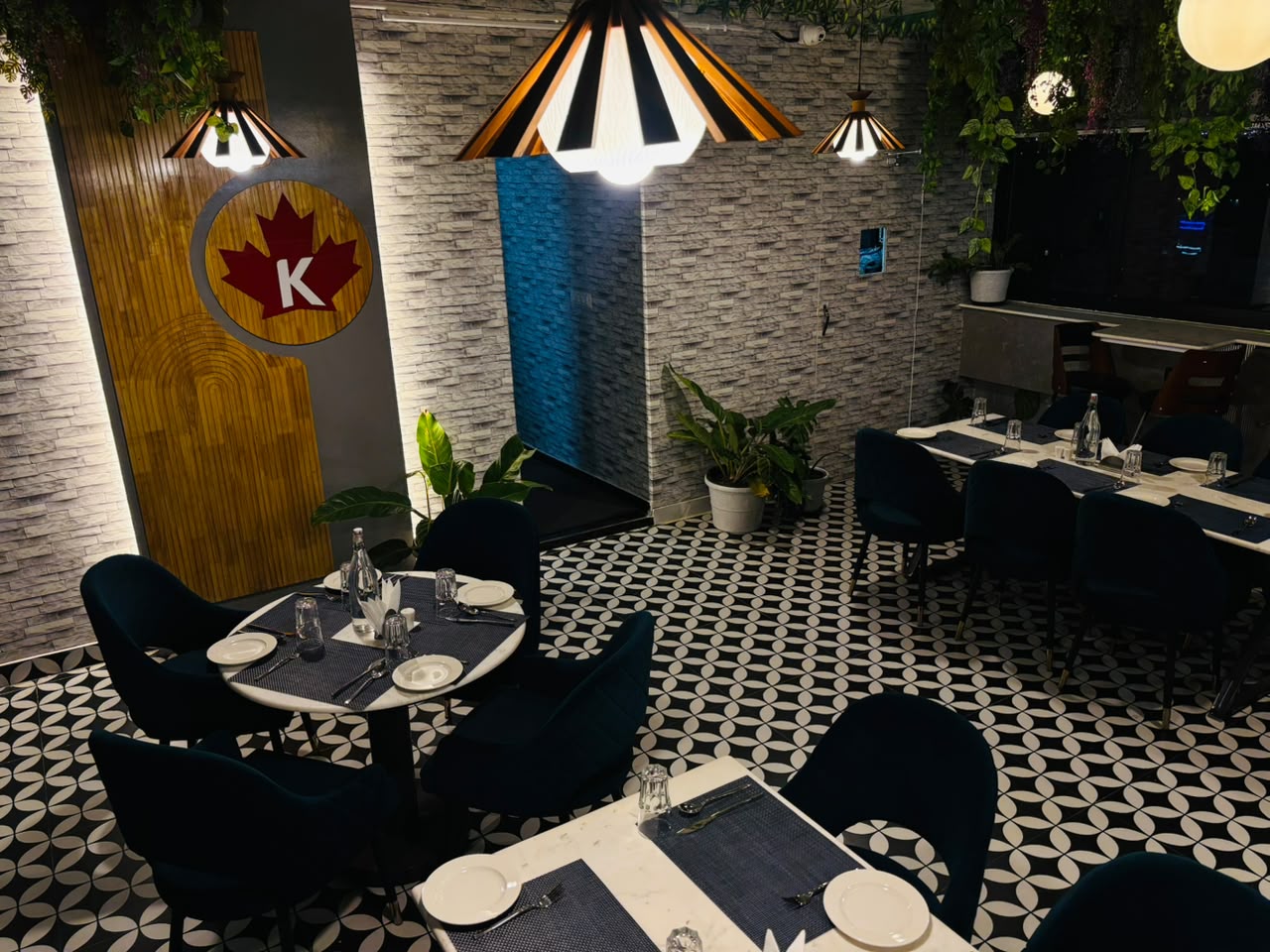 Restaurant dining area with patterned flooring, pendant lights, and greenery